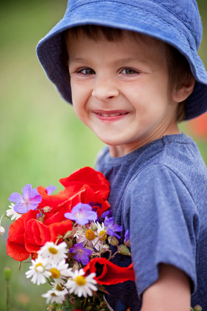 Cute kid boy with poppy flowers and other wild flowers in poppy field on warm summer day, nice soft evening lightの写真素材