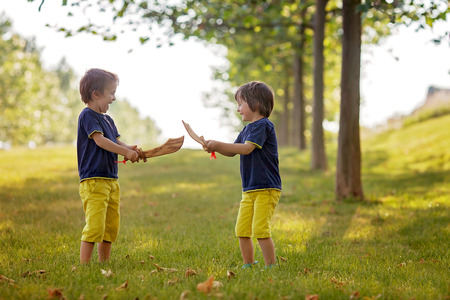 Two little boys, holding swords, glaring with a mad face at each other, fighting outdoors in the parkの写真素材