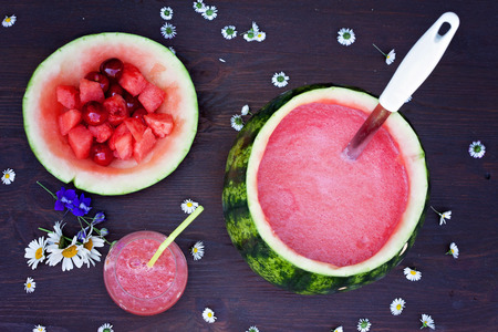 Fresh bowl of watermelon drink, drink in a glass and some fresh fruits on a brown wooden table background, daisy flowers on the tableの写真素材