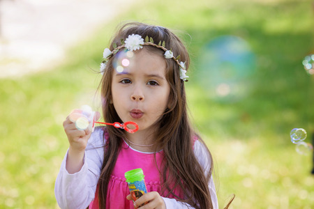 Beautiful portrait of sweet lovely little girl blowing soap bubbles in the park, summertimeの写真素材