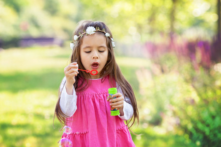 Beautiful portrait of sweet lovely little girl blowing soap bubbles in the park, summertimeの写真素材