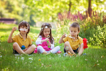 Three children in the park blowing soap bubbles and having fun, summer sunny dayの写真素材