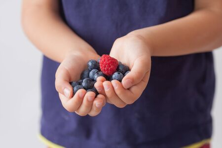 Child, holding raspberries and blueberries in his hands, isolated on whiteの写真素材