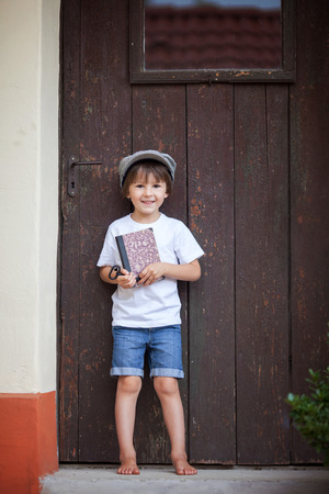 Cute little child, boy, holding big metal key and a book, willing to unlock a door, outdoorsの写真素材