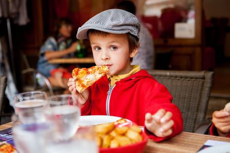 Sweet adorable child, boy, eating pizza at a restaurant, , summertime Sweet adorable child, boy, eating pizza at a restaurant, , summertime