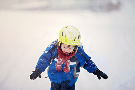 Happy little boy playing in the snow while snowing, helmet, scarf and glovesの写真素材