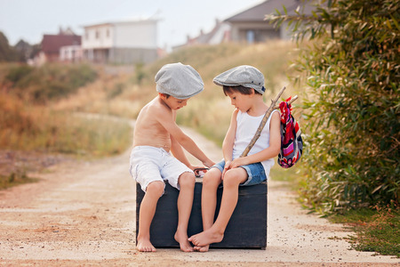 Two boys, sitting on a big old vintage suitcase, playing with marshmallow candies and talkingの写真素材