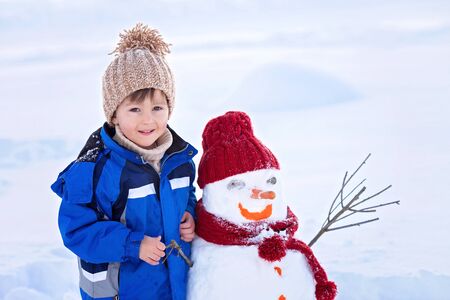 Happy beautiful child building snowman in garden, winter timeの写真素材