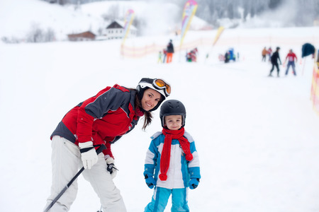 Beautiful young mom and her toddler boy, skiing in the mountains, winter timeの写真素材