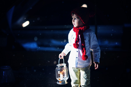 Sweet boy, holding a lantern, looking at a light coming through a window, standing in the snow, outdoorsの写真素材