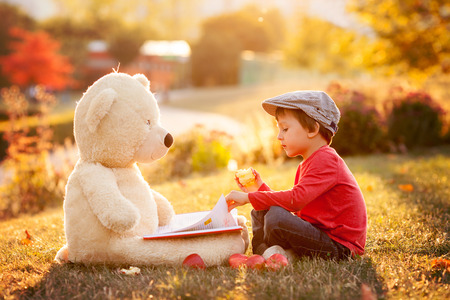 Adorable little boy with his teddy bear friend in the park on sunset, nice back lightの写真素材