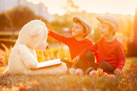 Two adorable little boys with teddy bear friend in the park on sunset, nice back lightの写真素材