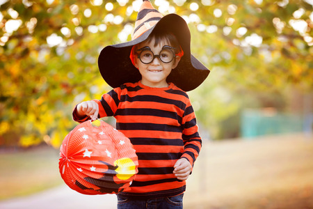 Cute boy in the park with halloween costume, hat and glasses, having fun autumn timeの写真素材