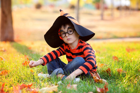 Cute boy in the park with halloween costume, hat and glasses, having fun autumn timeの写真素材
