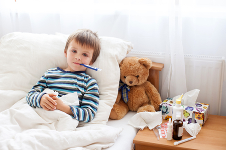 Sick child boy lying in bed with a fever, resting at home