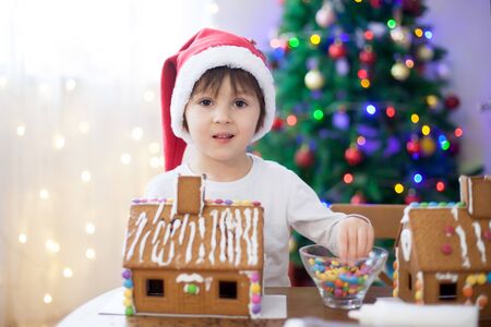 Cute little boy, making gingerbread cookies house, decorating at home in front of the Christmas tree, child playing and enjoying, Christmas conceptの写真素材