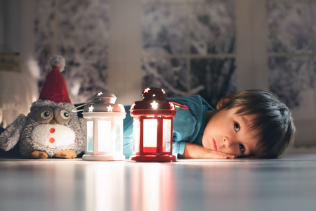 Beautiful little boy, lying down on the floor, looking at candles, making wishes for Christmasの写真素材