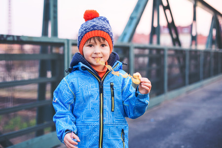 Cute boy, eating potato chips on a bridge, outdoors, wintertime