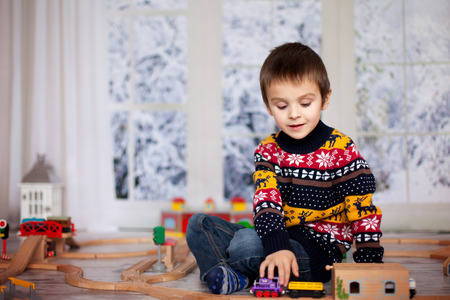 Adorable little preschool boy, playing with wooden trains and railroad at home, wintertime