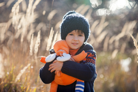 Cute little caucasian child, boy, holding fluffy toy, hugging it, in the park, on sunny winter dayの写真素材