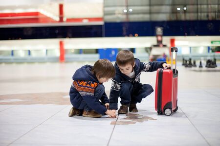 Two cute little sibling children, boys, at the airport, traveling together on Christmas