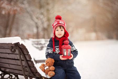 Cute little caucasian boy with teddy bear and red lantern, playing in the winter park, snowy dayの写真素材