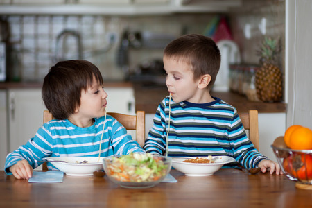 Two sweet children, boy brothers, having for lunch spaghetti at home, enjoying tasty foodの写真素材