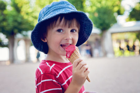 Cute little boy, eating big ice cream in the park, smiling at camera, summertimeの写真素材