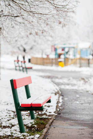 Red bench in a snowy park, children playground in the background, daytimeの写真素材