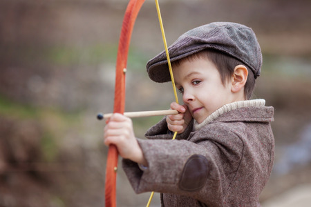 Adorable little preschool boy, shoot with bow and arrow at target in open air, springtime outdoors