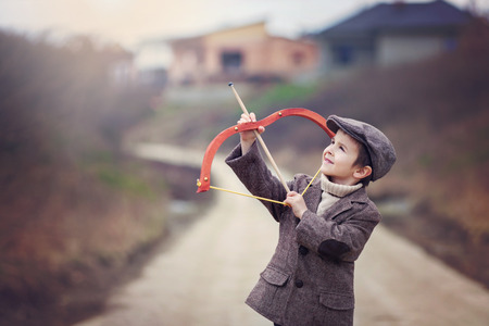 Adorable little preschool boy, shoot with bow and arrow at target in open air, springtime outdoorsの写真素材