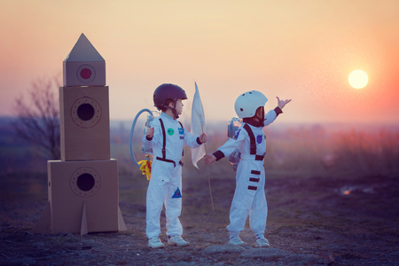 Two adorable children, boy brothers, playing in park on sunset, dressed like astronauts, imagining they are flying on the moonの写真素材