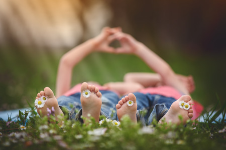 Happy little children, lying in the grass, barefoot, daisies around them, playing happily, childhood happiness conceptの写真素材