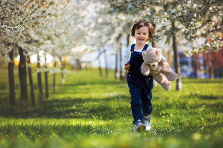 Cute little boy, eating strawberry in the park on a spring sunny afternoon, together with his big teddy bearの写真素材