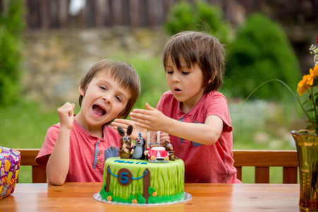 Beautiful adorable five year old boy, celebrating his birthday, blowing candles and eating the cake, outdoors. Birthday party for kidsの写真素材