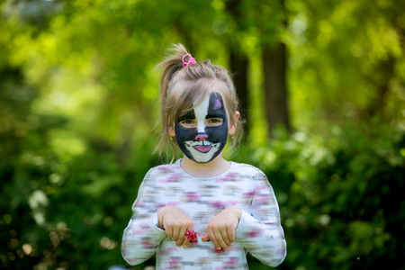 Cute little five years old girl, having her face painted as kitten on her birthday party, outdoorsの写真素材