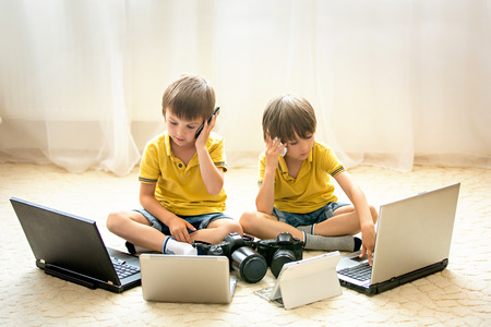 Two boys, preschool children, having fun playing at home with computers and talking on the phone