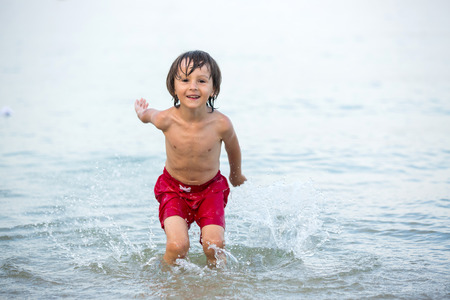 Cute boy, splashing water on the beach, having funの写真素材
