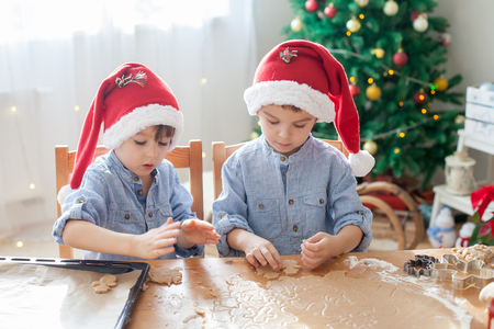 Two cute boys with santa hat, preparing cookies at home, Christmas tree behind themの写真素材