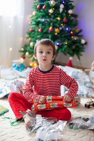 Two sweet children, boy brothers, opening presents on Christmas day, still in pajamas. Kids...