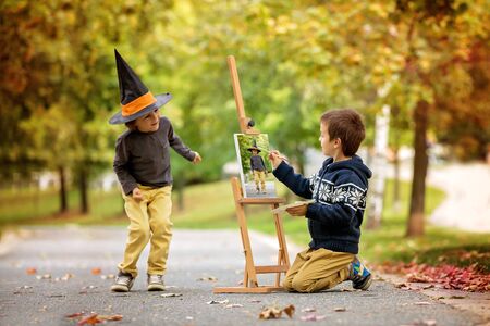 Two sweet children, boy brothers, having fun painting in autumn park together. One child paint the other kid, dressed for halloweenの写真素材
