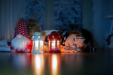 Beautiful little boy, lying down on the floor, looking at candles, making wishes for Christmasの写真素材