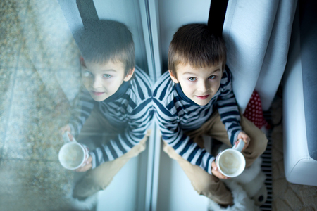Adorable little preschool child, boy, drinking milk, sitting on window shield, reflecting on the windowの写真素材