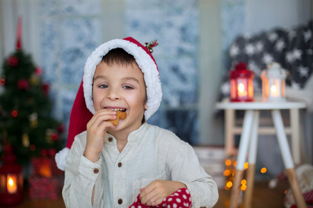 Cute preschool child, boy, reading a book and eating cookies at home, while snowing outdoorsの写真素材