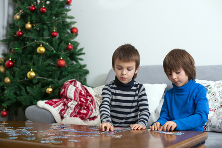 Two sweet children, collect puzzles at home sitting on a couch on Christmasm christmas decoration behind themの写真素材