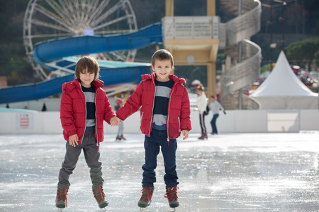 Happy children, boys, brothers with red jackets, skating during the day, having funの写真素材