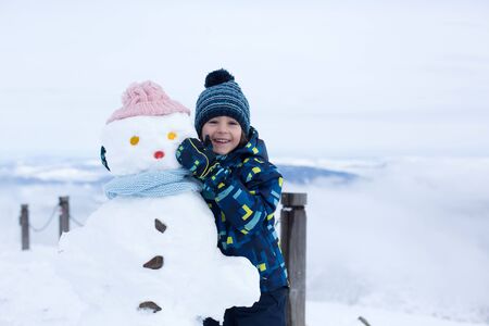 Cute child, building snowman and playing with it on top of mountain, wintertimeの写真素材