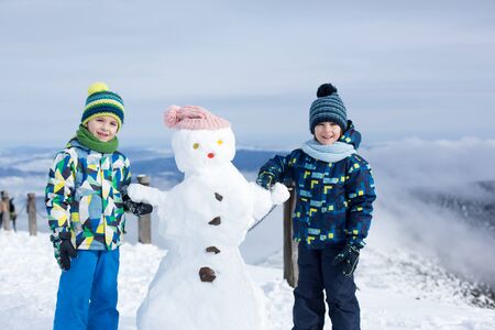Two children, building snowman on top of mountain, wintertimeの写真素材