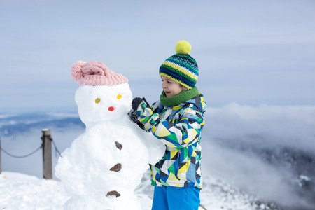 Two children, building snowman on top of mountain, wintertimeの写真素材