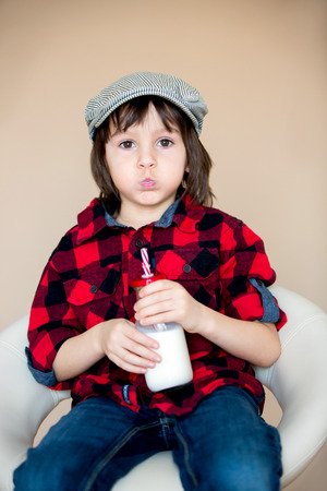 Beautiful fashionable little preschool boy, drinking milk from bottle, isolated imageの写真素材
